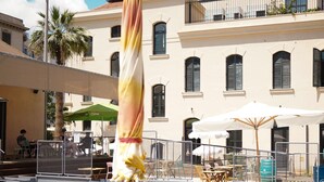A poolside area with lounge chairs and umbrellas, a building with a sign reading "Ostello Bello," and a clear blue sky. - Ostello Bello Palermo  (Palermo)