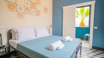 Un lit bien fait, avec une couvre-lit bleue et des oreillers blancs, une table de chevet avec une lampe, et un motif décoratif sur le mur.