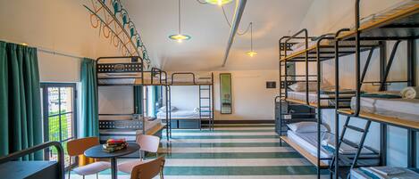 A dormitory room with bunk beds, a dining table with chairs, and a view of the city through the window.
