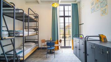 A dormitory room with bunk beds, a small table with chairs, and a kitchenette area.