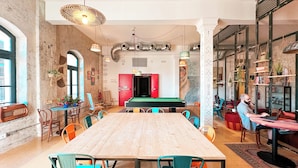 A spacious dining area with a long wooden table, colorful chairs, and a pool table in the background. - Ostello Bello Palermo  (Palermo)