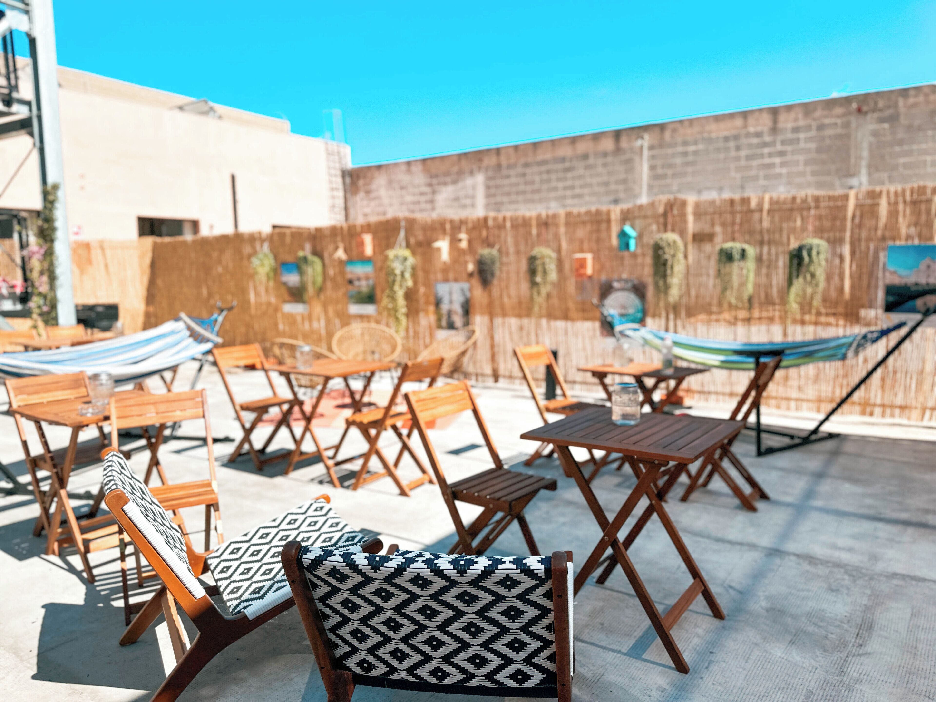 An outdoor seating area with wooden chairs and tables, a hammock, and a brick wall with greenery.