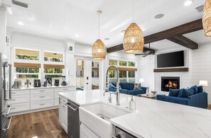 A modern kitchen with white cabinetry, a large island, and a dining area with blue sofas. - Ciao Bella | Steps from the Beach | Golf Cart 🛺 (Santa Rosa Beach)
