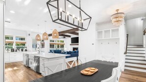 A modern kitchen with white cabinets, a black dining table, and a chandelier.