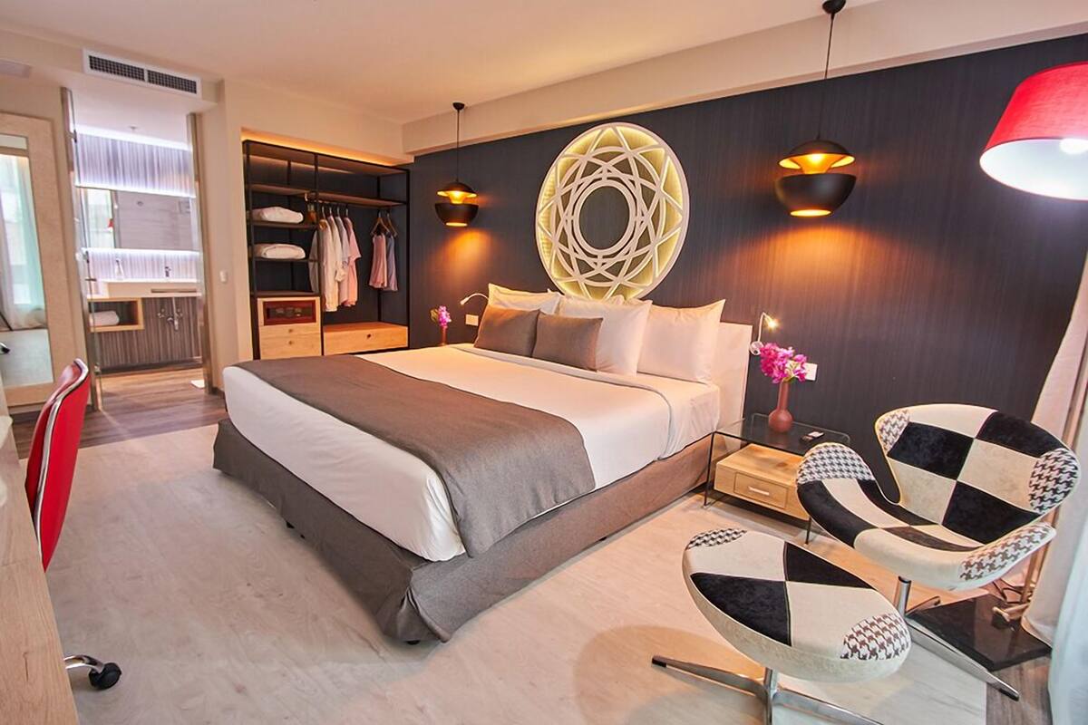 Een moderne slaapkamer met een groot bed, een inloopkast en een zithoek met twee stoelen.
