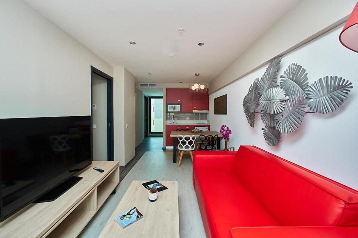 Un salon moderne avec un grand téléviseur à écran plat, un canapé rouge et une table basse sur laquelle sont posés des magazines.