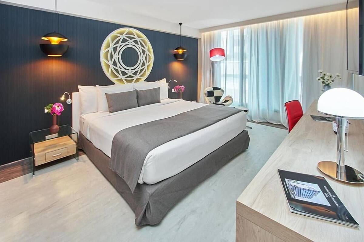 Een moderne hotelkamer met een groot bed, een bureau met lamp en een decoratief wandobject.
