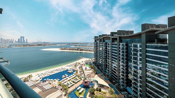 A high-rise hotel overlooking a beach with a marina, pool, and resort area.