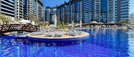 A swimming pool with lounge chairs and umbrellas, surrounded by high-rise buildings.