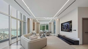 A modern living room with a large sofa, a dining area, and a TV mounted on the wall.