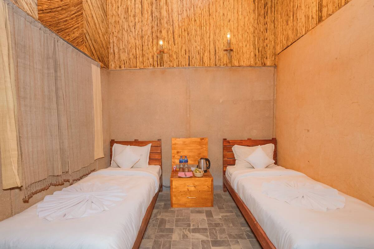 A room with two beds, a wooden nightstand, and a woven ceiling.