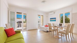 A bright living room with a green sofa, a dining table with chairs, and a balcony with a view. - 3951 Mono di Annahouse by Barbarhouse (Porto Cesareo)