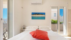 A bedroom with a bed, white pillows, a red pillow, a nightstand with a lamp, and a painting of a beach scene. - 3951 Mono di Annahouse by Barbarhouse (Porto Cesareo)