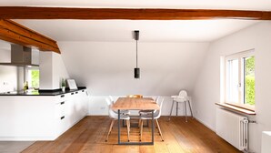 Une cuisine moderne avec des meubles blancs, une table à manger en bois et une vue sur la verdure à l’extérieur.