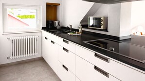 Une cuisine moderne avec des armoires blanches, un comptoir noir, un four à micro-ondes encastré et une fenêtre donnant sur un paysage verdoyant.