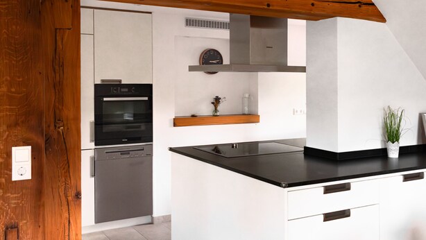 Une cuisine moderne avec des meubles blancs, un plan de travail noir et un plafond en bois.