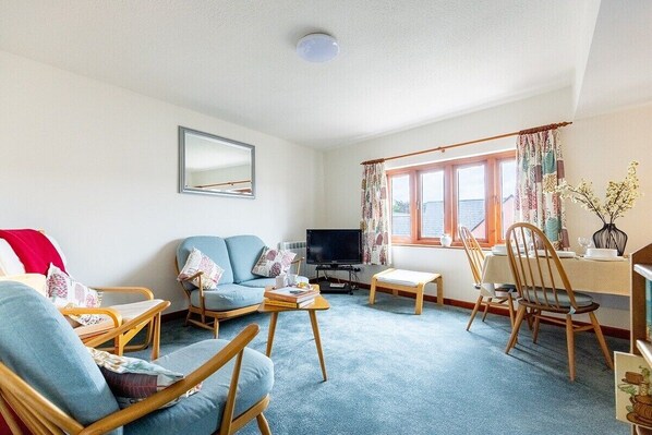 A living room with a sofa, chairs, a television, and a dining area with a table and chairs.