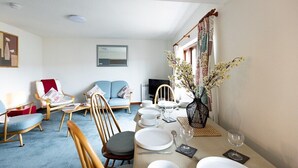 A dining area with a table set for four, surrounded by chairs, a sofa, and a television.