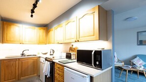 A compact kitchen with wooden cabinets, a microwave, a toaster, and a small refrigerator.