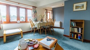 A cozy room with a dining table, chairs, a bench, a bookshelf, and a window with curtains.
