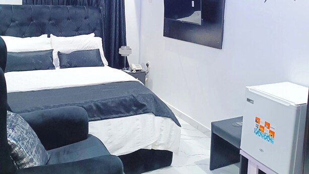 A modern bedroom with a bed, bedside table, air conditioning unit, and a clock on the wall. - Blueocean.cog Apartments (Benin City)