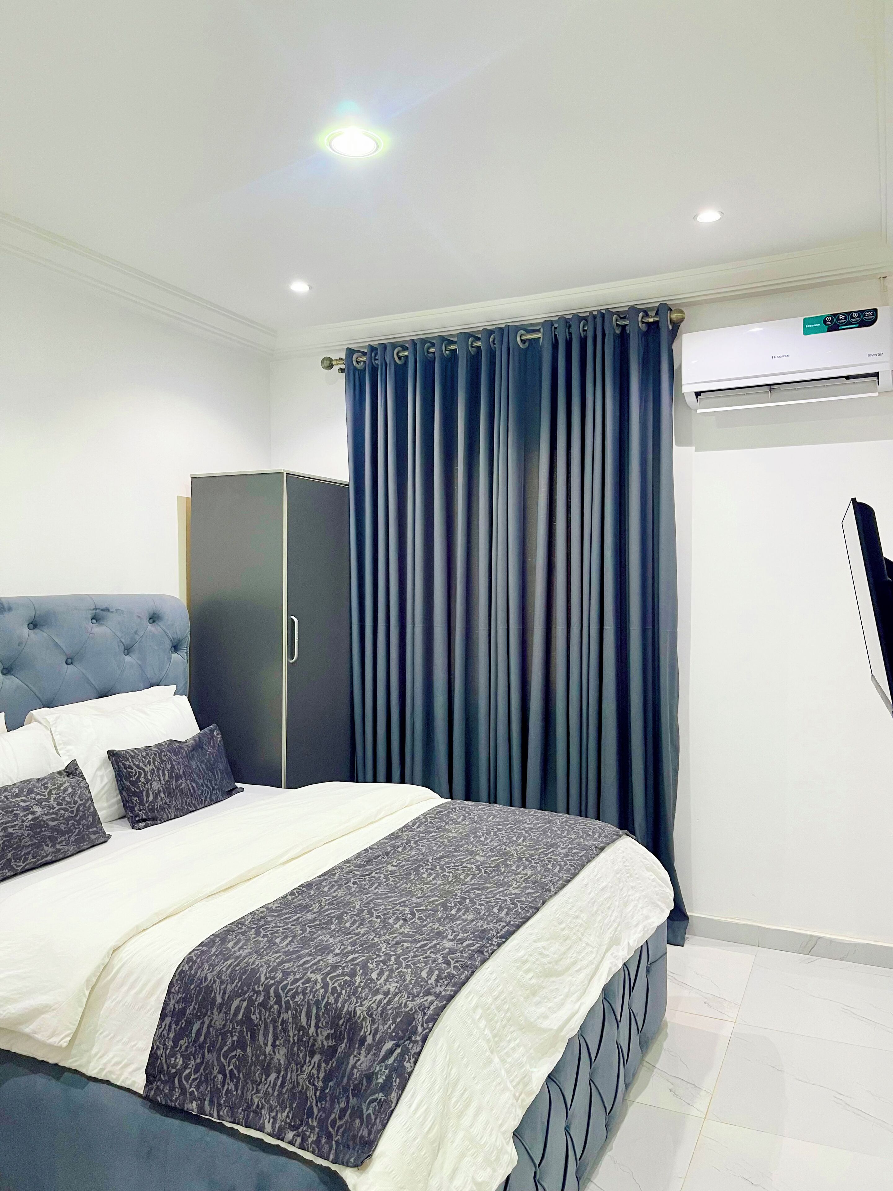 A modern bedroom with a bed, a wardrobe, a flat-screen TV, and an air conditioning unit.