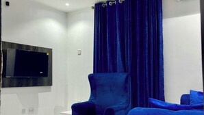 A modern living room with a white sofa, a blue armchair, a white coffee table, and a pink chandelier. - Blueocean.cog Apartments (Benin City)