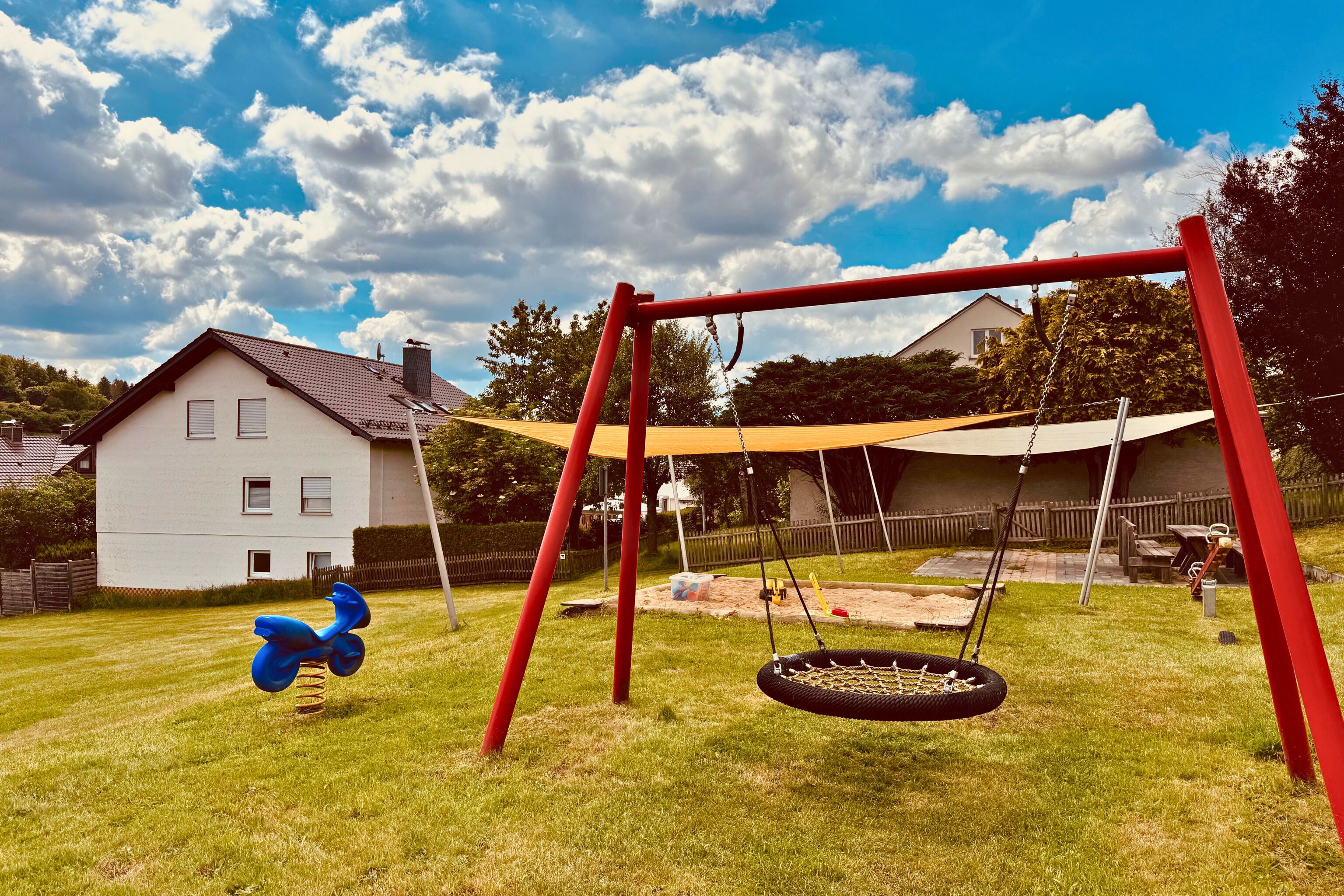 A swing set with a tire swing and a scooter in a backyard with a house in the background.