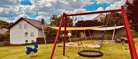 A swing set with a tire swing and a scooter in a backyard with a house in the background.