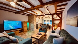 A cozy living room with a television, wooden furniture, and a stone wall. - Large Holiday Home for Groups up to 17 Guests with Hot Tub & Playroom (Herbstein)