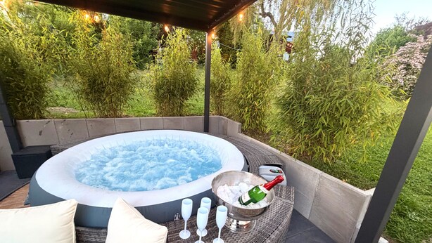 A hot tub with a wicker table and cushions, surrounded by greenery. - Large Holiday Home for Groups up to 17 Guests with Hot Tub & Playroom (Herbstein)