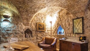 Una habitación rústica con paredes de piedra, una mesa de madera, un sillón de cuero y un armario.