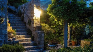 Una escalera de piedra que conduce a una fuente de luz, rodeada de follaje y plantas en macetas.