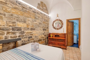 A room with a stone wall, a wooden dresser, a bed with a striped bedspread, and a framed picture on the wall. - Caratteristico Appartamento In Centro (Sanremo)