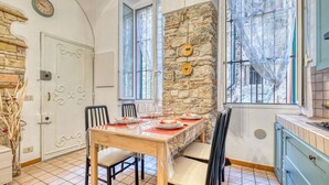 A dining area with a stone wall, a wooden table set for four, and a kitchen area with blue cabinets. - Caratteristico Appartamento In Centro (Sanremo)