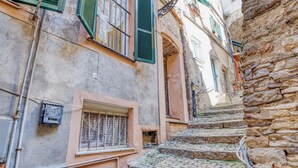 A narrow stone staircase leading to a building with a rustic facade, a small window with a metal grille, and a utility box attached to the wall. - Caratteristico Appartamento In Centro (Sanremo)
