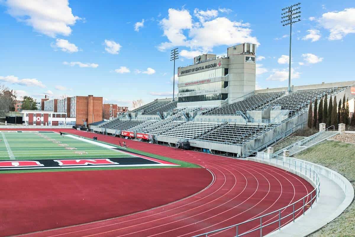 Een stadion met een atletiekbaan, tribunes en een gebouw met bewegwijzering.