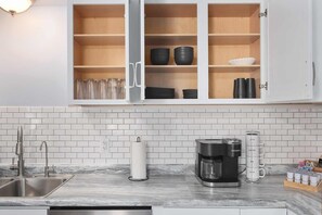 A kitchen with white cabinets, a marble countertop, a coffee maker, and a kettle.