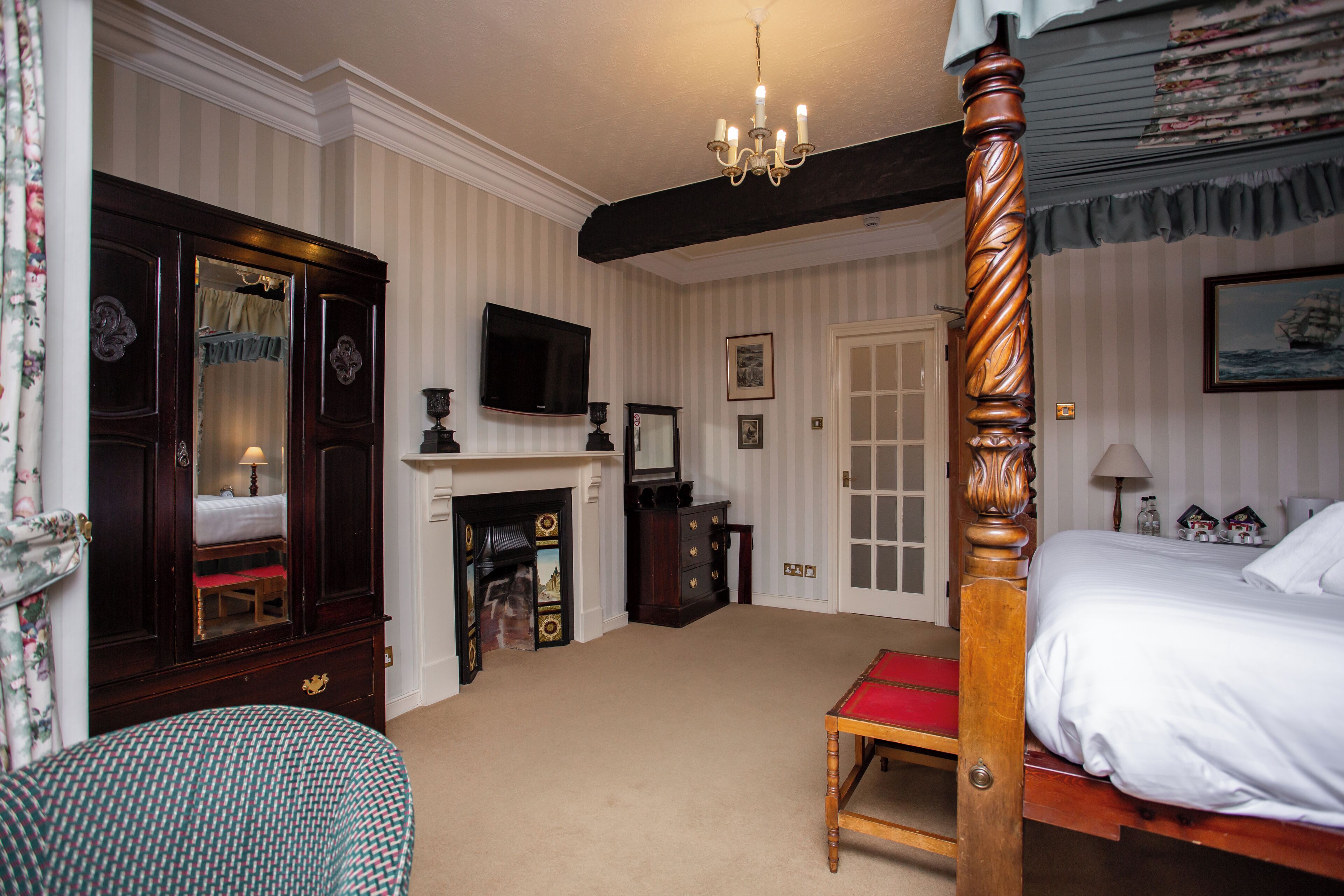 A room with a four-poster bed, a television, a fireplace, and a large mirror.