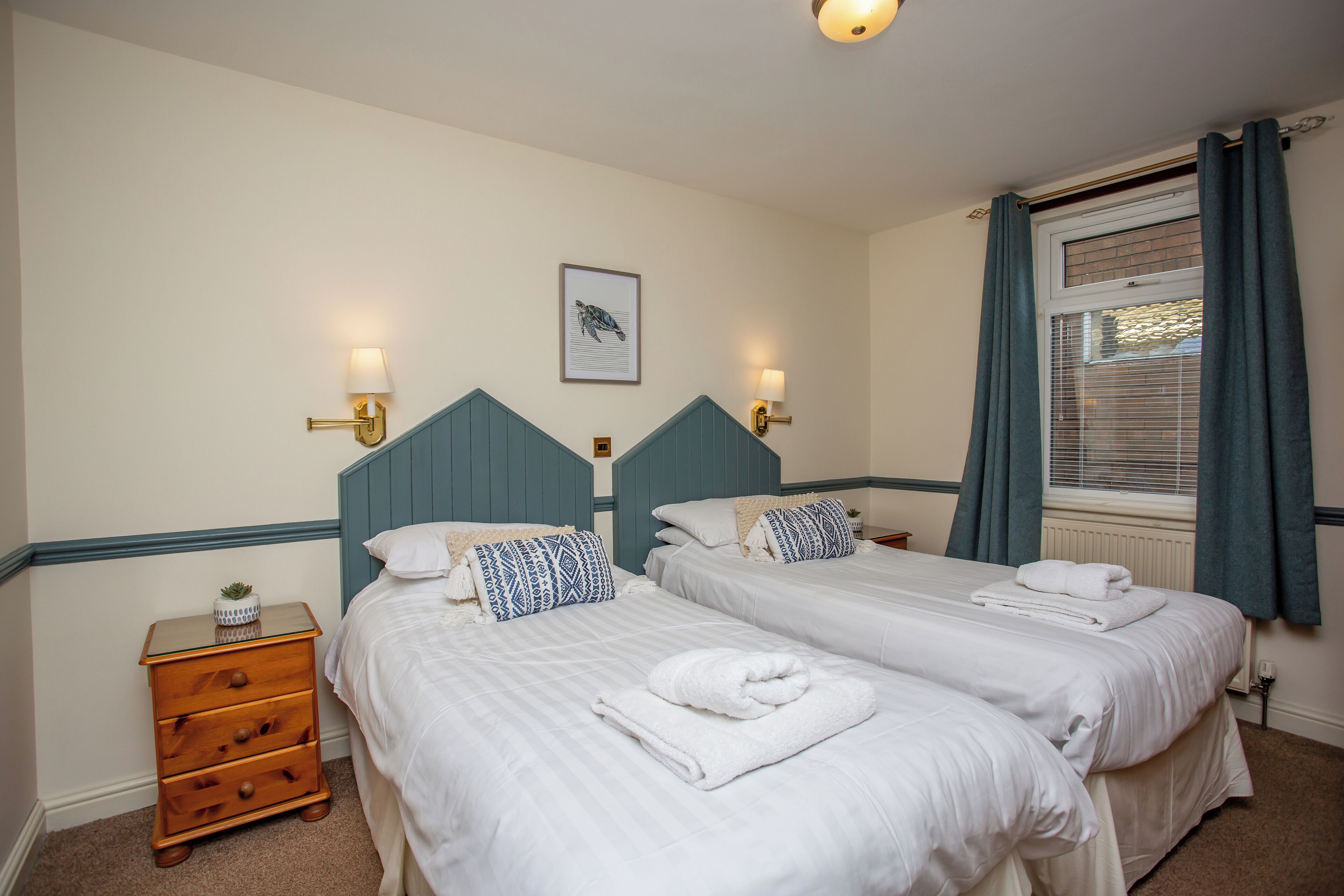 A hotel room with two beds, a nightstand, and a window with curtains.