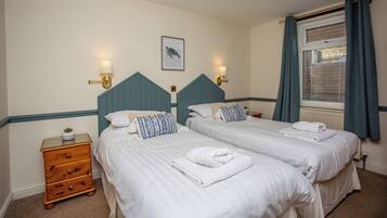 A hotel room with two beds, a nightstand, and a window with curtains.