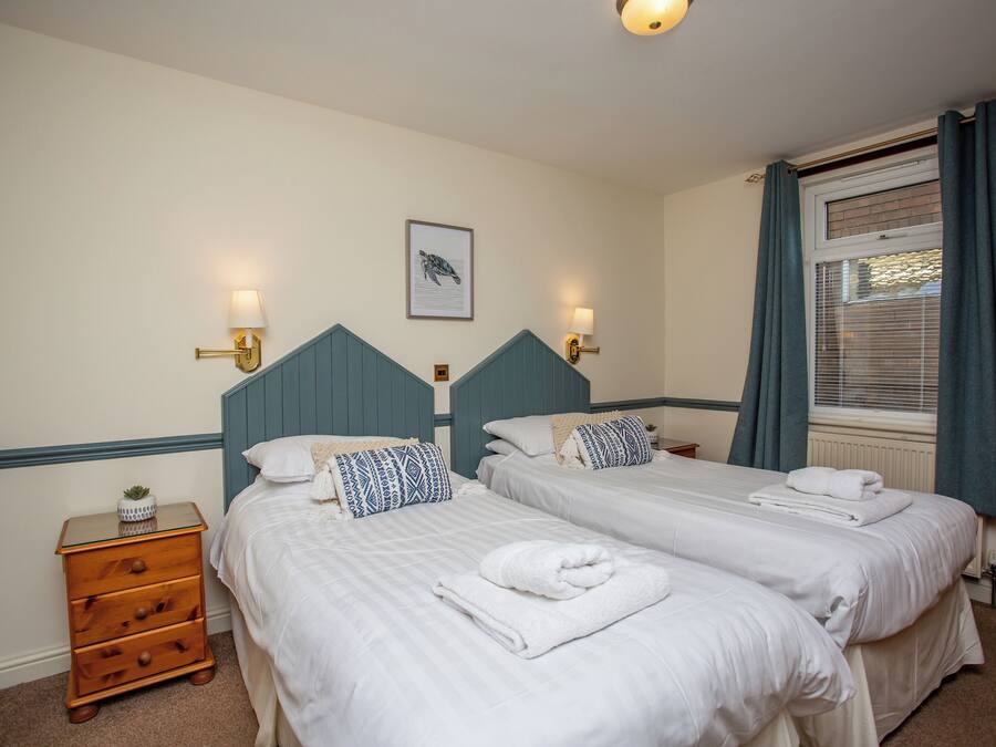A hotel room with two beds, a nightstand, and a window with curtains.