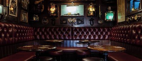 A vintage bar with leather booths, wooden tables, and brass fixtures.