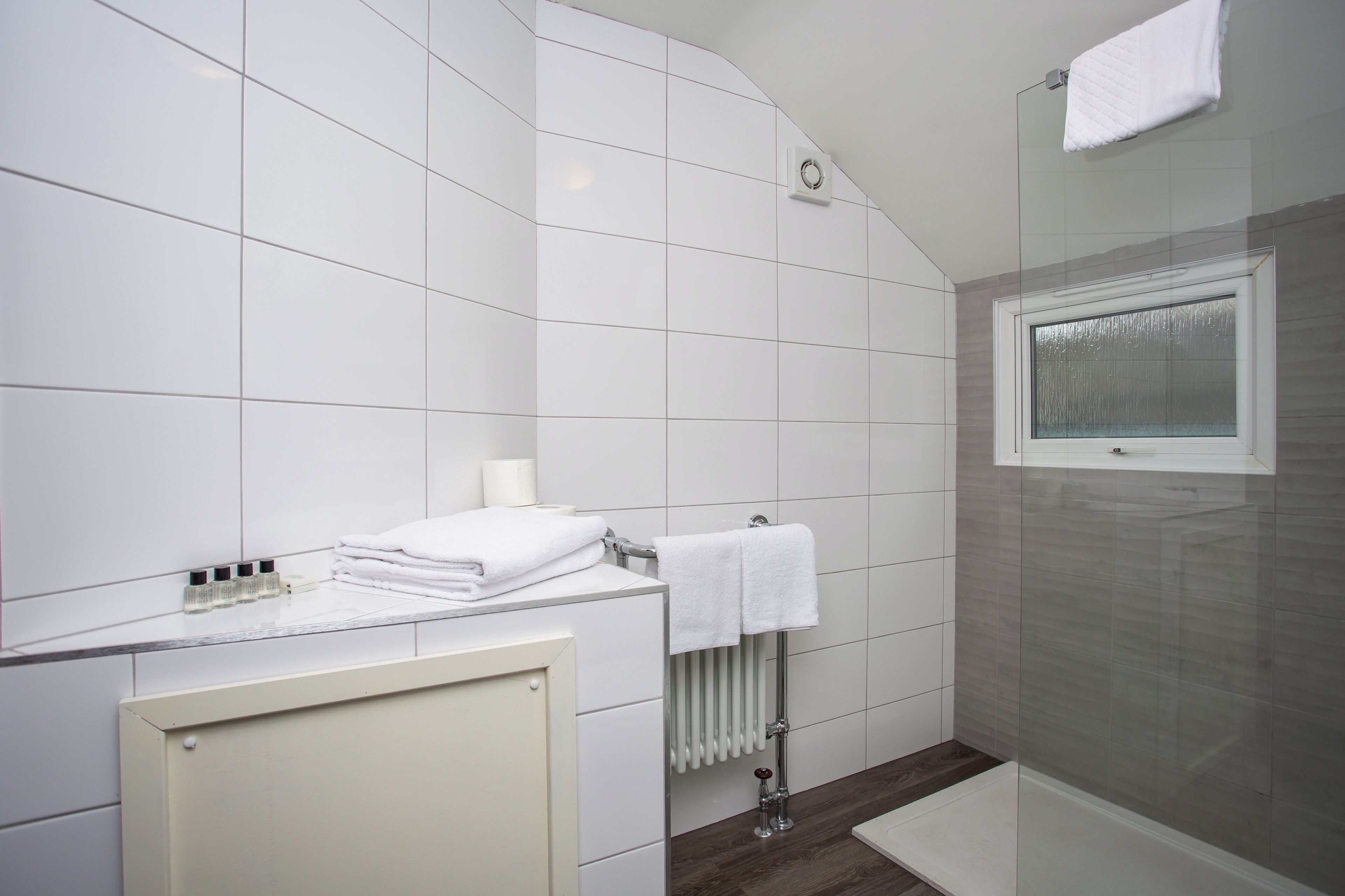 Un baño moderno con azulejos blancos, cabina de ducha de vidrio y una toalla blanca sobre el mostrador.