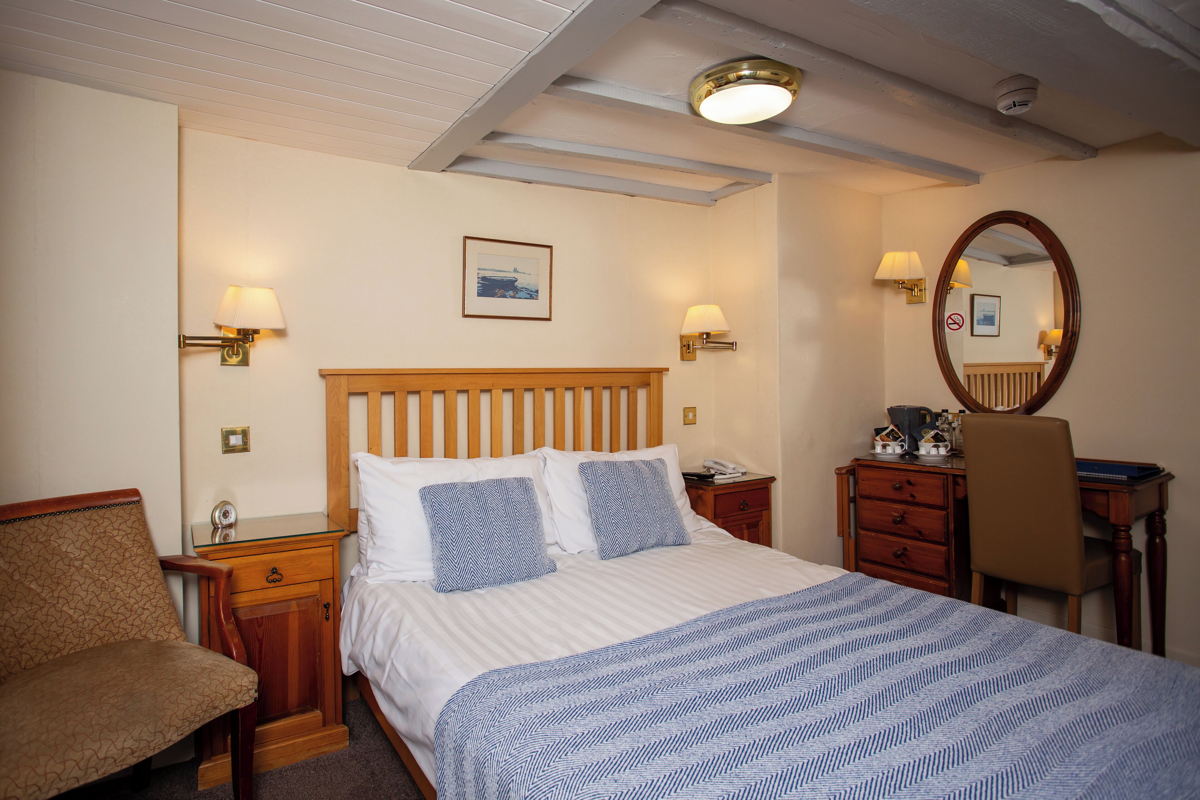 A hotel room with a bed, bedside tables, a chair, a desk, a mirror, and a lamp.