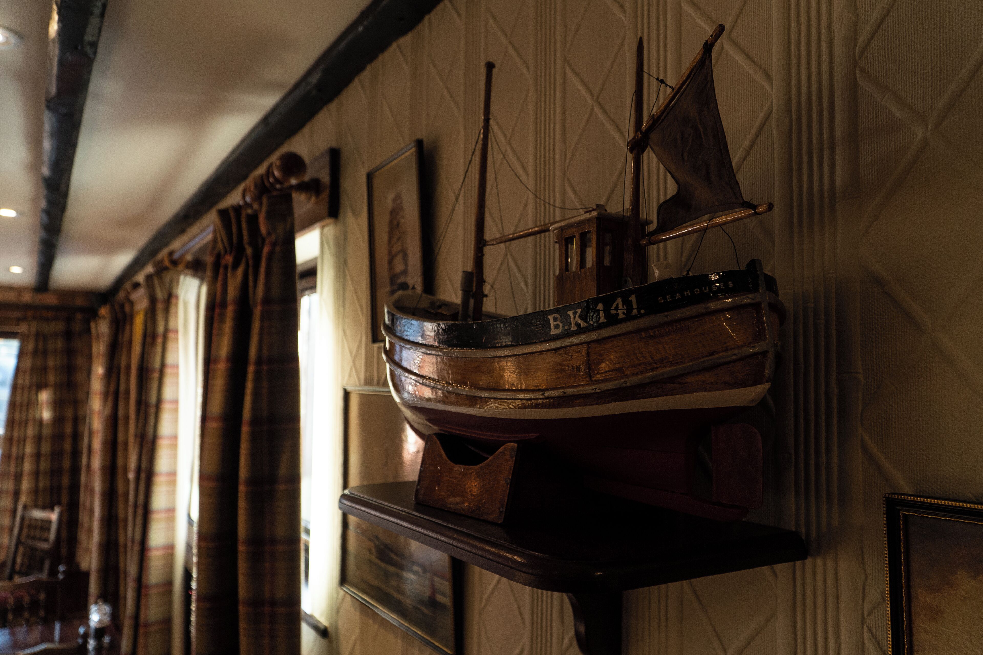A model ship mounted on a wall in a room with patterned wallpaper and wooden beams.