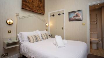A neatly made bed with white linens, a bedside table with a lamp, and a framed picture on the wall.