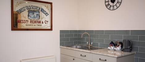 A kitchen with a sink, countertop, and a clock on the wall.