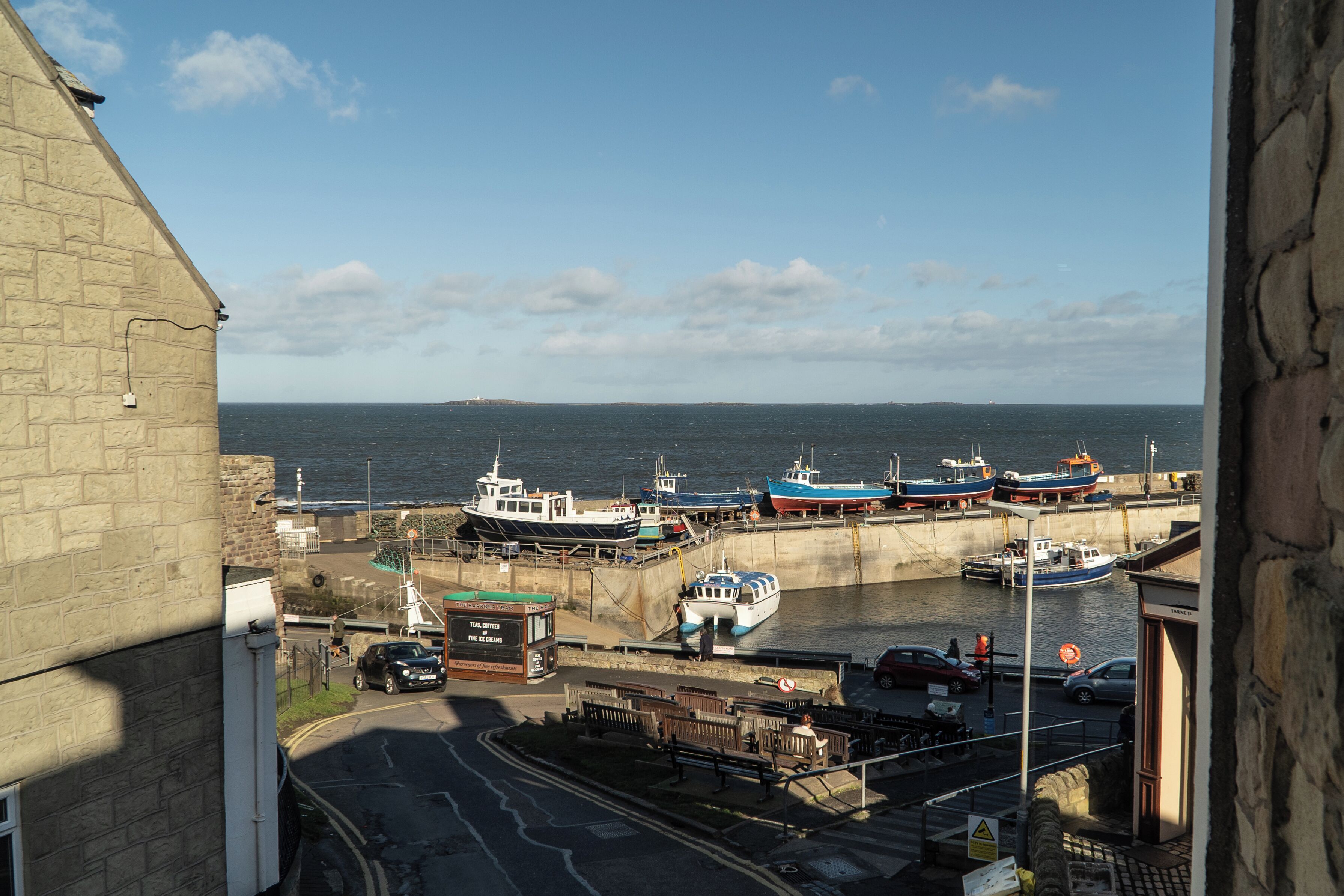 A harbor with boats docked, a road, and a building with stone walls.