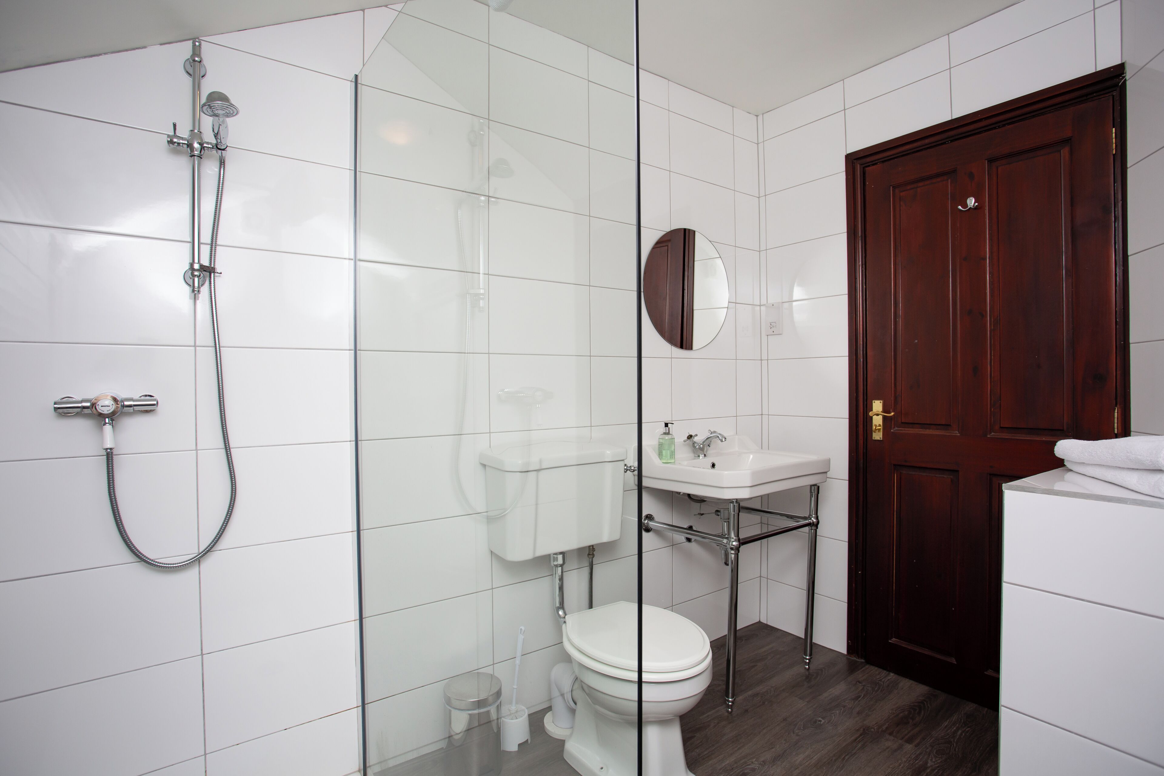 A modern bathroom with a glass shower enclosure, a white toilet, a sink with a mirror, and a wooden door.